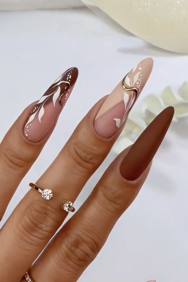 Artistic matte nail designs featuring intricate floral patterns in earthy tones and elegant finishes.